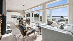 Amplia sala de estar con un ventanal que ofrece vistas panorámicas, un comedor con mesa de madera y una cocina con alacenas blancas.