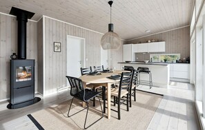 Una cocina moderna con armarios blancos, un comedor con mesa y sillas de madera, y un estufa de leña negra.
