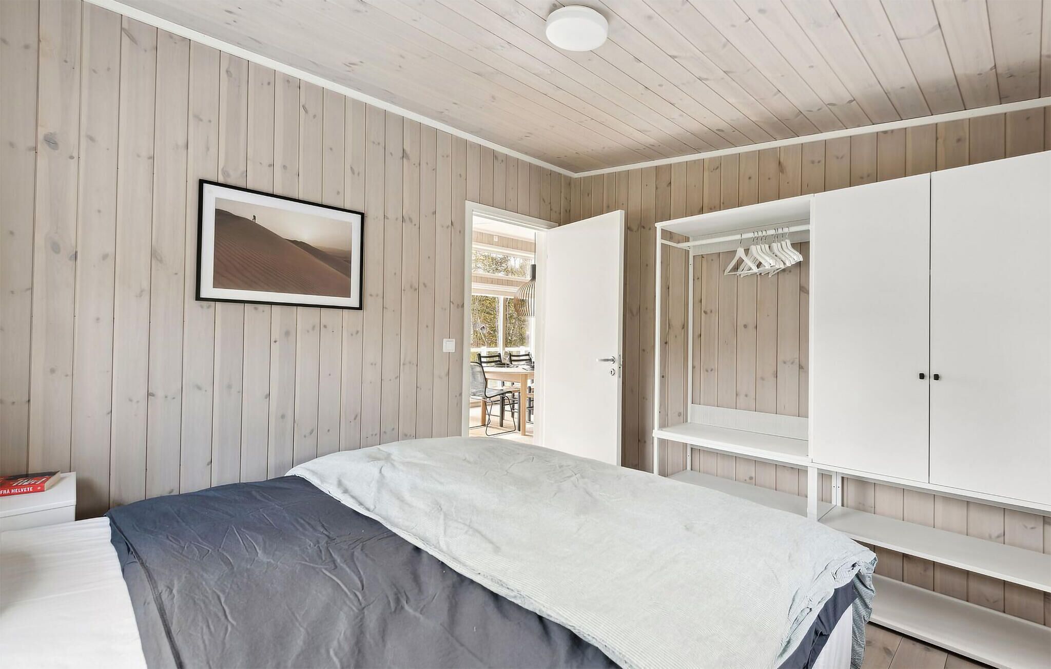 A bedroom with a bed, a wardrobe, a framed picture, and a door leading to a balcony.