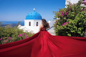 Eine Person in einem roten Kleid steht vor einem weißen Gebäude mit einer blauen Kuppel, umgeben von Grünpflanzen und Blumen.