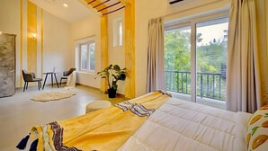Un dormitorio con cama, balcón, zona de comedor y vistas a zonas verdes.