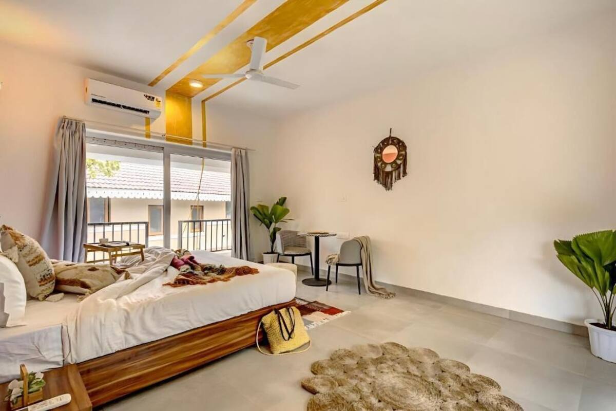 Un dormitorio con cama, mesita de noche, silla, planta en maceta y ventilador de techo.