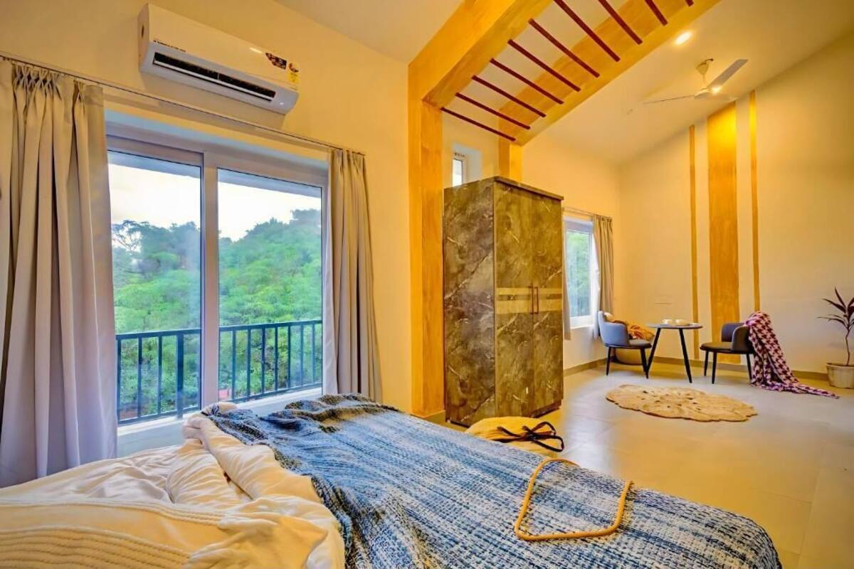 Un dormitorio con un ventanal grande, una cama, un armario, una mesita y una silla.