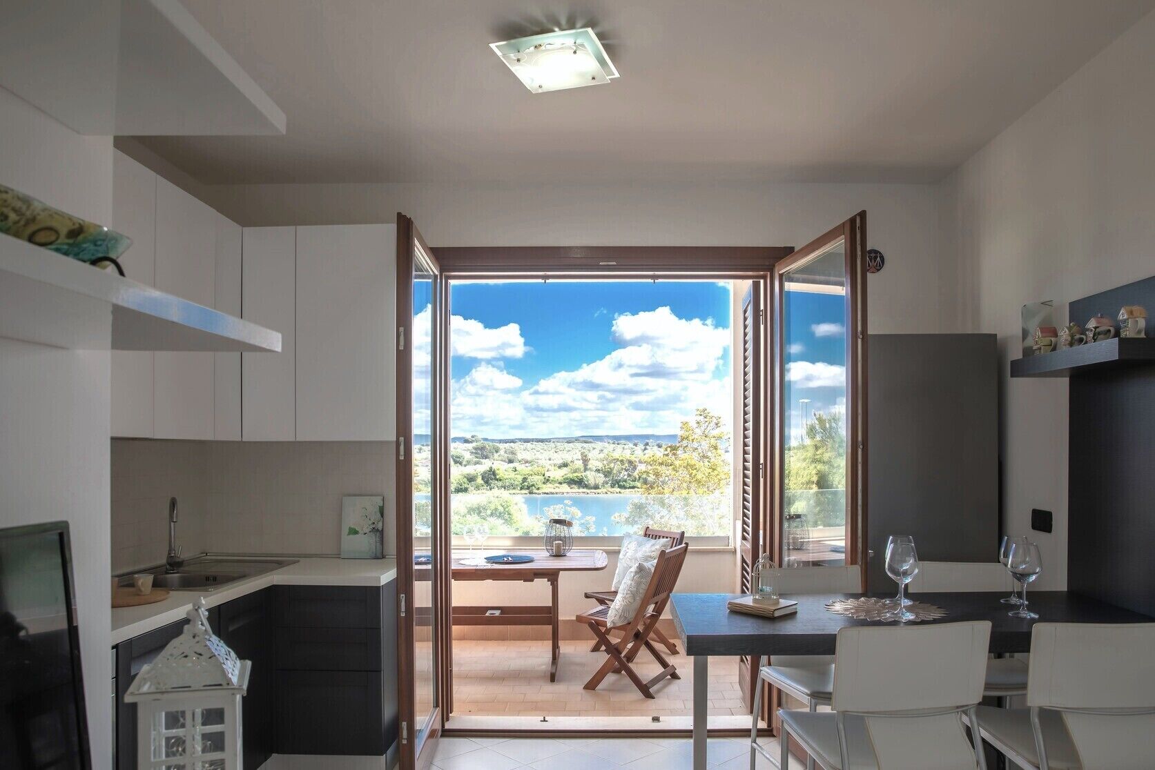 Eine moderne Küche mit Seeblick und Hügeln, ein Essbereich mit Tisch und Stühlen sowie ein kleiner Balkon mit Tisch und Stühlen.