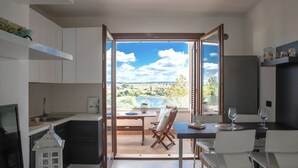 Une cuisine moderne avec vue sur un lac et des collines, un coin repas avec une table et des chaises, et un petit balcon également équipé d’une table et de chaises.