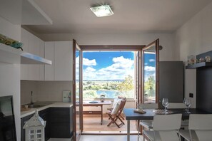 Eine moderne Küche mit Seeblick und Hügeln, ein Essbereich mit Tisch und Stühlen sowie ein kleiner Balkon mit Tisch und Stühlen.