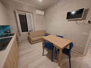 Un espace de vie compact comprenant un coin cuisine, un canapé, une table à manger et un téléviseur fixé au mur.