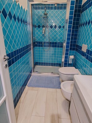 Une salle de bain avec des murs recouverts de carreaux bleus, une douche, des toilettes et une baignoire.