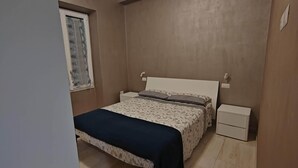 A bedroom with a bed, bedside tables, a window with curtains, and a ceiling light fixture. - Gozzi's Den - Alghero (Alghero)