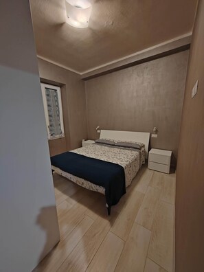 Ein Schlafzimmer mit Bett, Nachttischen, einem Fenster mit Vorhängen und einer Deckenleuchte.