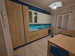 Eine Küche mit Holzausstattung, blauer Spritzschutzwand, einem Spülbecken, einem Herd und einem Essbereich mit Tisch und Stühlen.