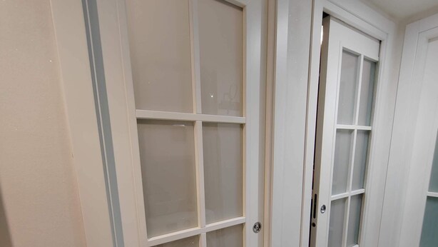 A hallway with two white doors with frosted glass panels, a light-colored tiled floor, and a plain wall. - Gozzi's Den - Alghero (Alghero)