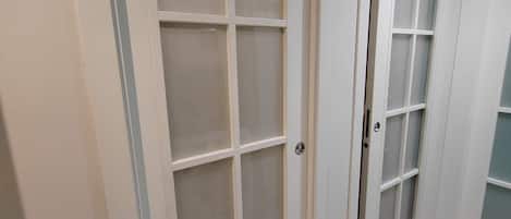 A hallway with two white doors with frosted glass panels, a light-colored tiled floor, and a plain wall.