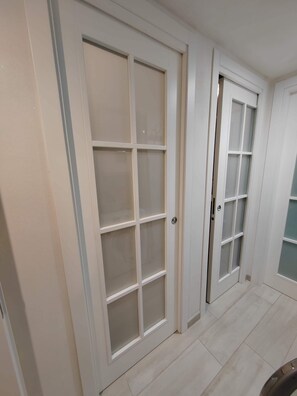 Ein Flur mit zwei weißen Türen mit gefrosteten Glasscheiben, einem hellen Fliesenboden und einer schlichten Wand.