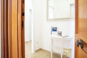 A hallway with a white wall, a wooden door, and a white console table with a mirror and brochures. - Infinite Blue View-Alghero (Alghero)