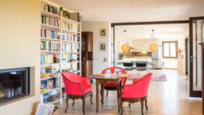 Ein Wohnzimmer mit Bücherregal, ein Essbereich mit Tisch und Stühlen sowie eine Küche im Hintergrund.