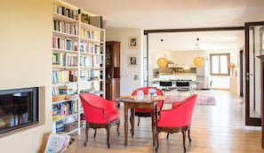 Ein Wohnzimmer mit Bücherregal, ein Essbereich mit Tisch und Stühlen sowie eine Küche im Hintergrund.