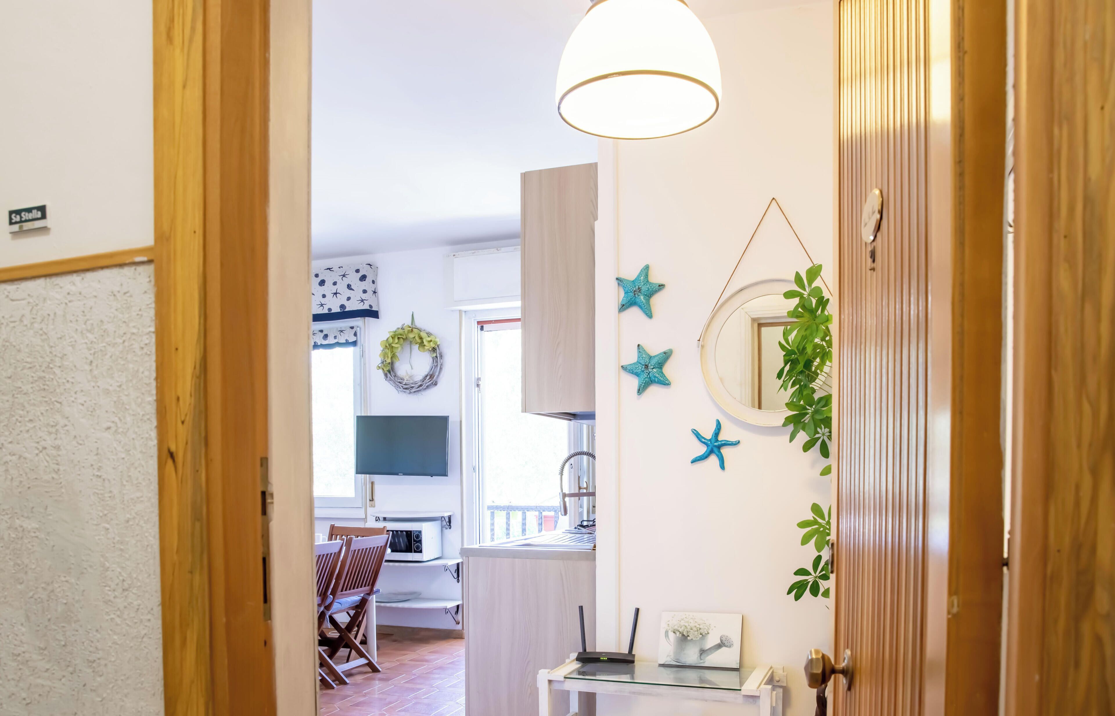 A hallway with a wooden door, a white wall, and a view into a room with a dining table and chairs.