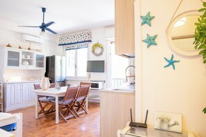 A modern kitchen with white cabinets, a dining table with chairs, a ceiling fan, and decorative starfish on the wall. - Alghero Sa Stella Holiday Home (Alghero)