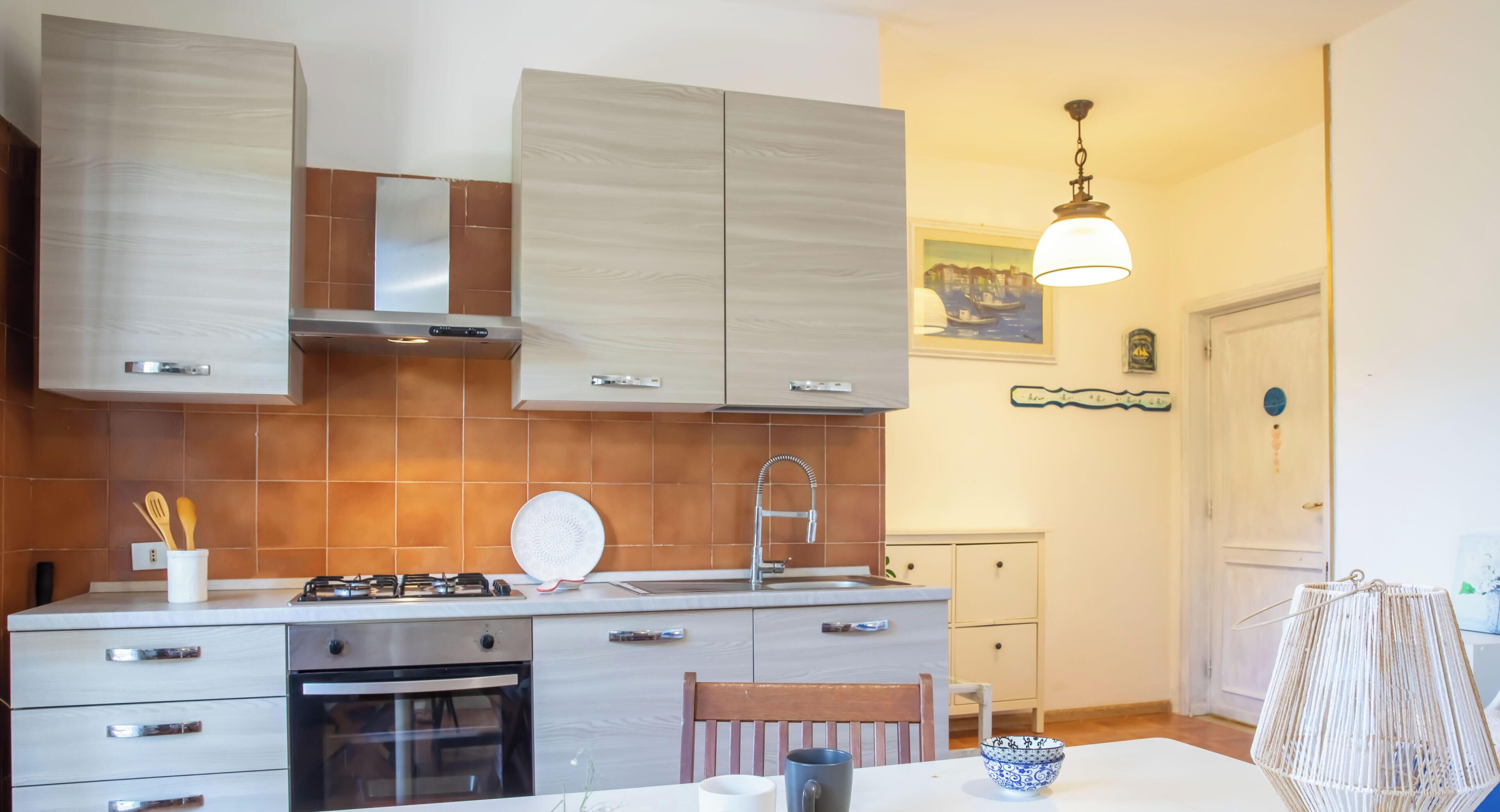 A modern kitchen with a stove, oven, and cabinets, a dining area with a table and chairs, and a hanging light fixture.