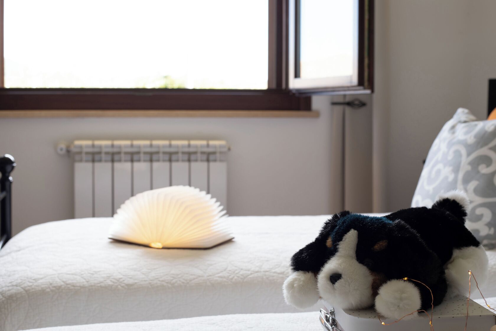 Un letto con una coperta bianca a trama decorativa, un termosifone bianco e una finestra vista sul verde.