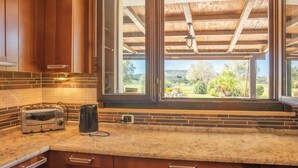 A kitchen with a toaster, a kettle, and a window overlooking a garden. - Villa Monica - Alghero (Alghero)
