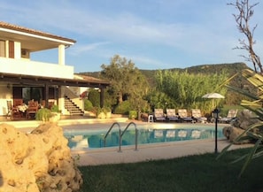 Ein Poolbereich mit Liegestühlen, ein Gebäude mit Balkon und eine Treppe, die zu der oberen Etage führt.