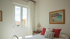 Une chambre à coucher avec un lit, une table de chevet, une lampe, une fenêtre avec des rideaux et un tableau au mur.