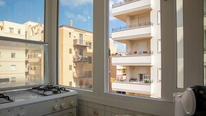 Une cuisine équipée d’une cuisinière à gaz, une fenêtre donnant sur des immeubles d’habitation et une table avec deux tasses.