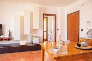 A modern living room with a sofa, a wooden table with decorative items, a television, and a door leading to a laundry area. - Red Coral Loft-Alghero (Alghero)
