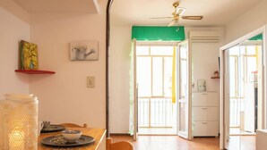 Un comedor con una mesa, sillas, un ventilador de techo y vistas al balcón exterior a través de un ventanal.