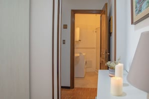 Ein Flur, der zu einem Badezimmer mit Toilette, Waschbecken und Dusche führt. Auf einem Tisch stehen Kerzen.