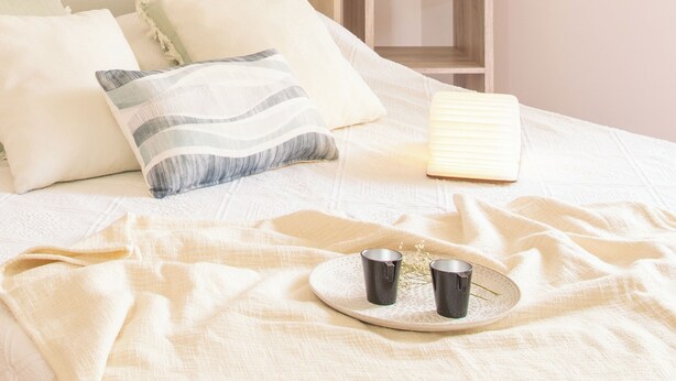 Una cama con almohadas, una mesita de noche con una lámpara y una bandeja con dos tazas.