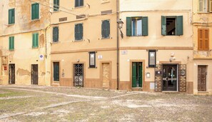 A building with multiple doors and windows, some with shutters, and a cobblestone ground. - Suite Porto antico - Alghero (Alghero)