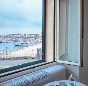 A room with a large window overlooking a marina with boats and a cityscape. - Suite Porto antico - Alghero (Alghero)