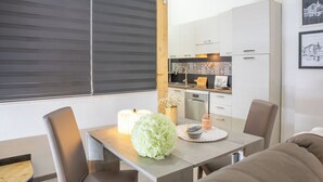 Une cuisine moderne avec des meubles blancs, une table à manger avec des chaises et une fenêtre avec des stores.