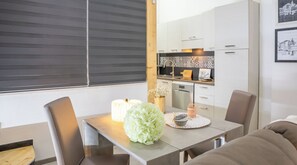 Eine moderne Küche mit weißen Schränken, einem Esstisch mit Stühlen und einem Fenster mit Jalousien.
