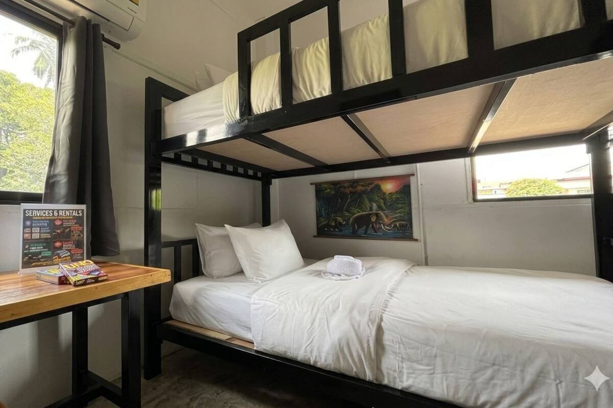 A bunk bed room with a wooden desk, a painting on the wall, and a window with a view of trees.