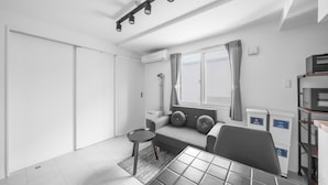 Una sala de estar moderna y minimalista con un sofá, una mesita redonda, una mesa de centro, una ventana con cortinas y un equipo de aire acondicionado empotrado.
