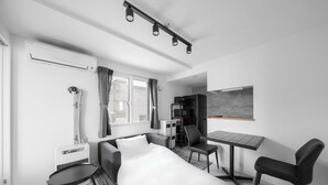 Una habitación de hotel moderna con cama, escritorio, dos sillas, equipo de aire acondicionado y una pequeña mesa.