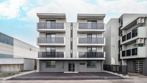 Un edificio moderno de varios pisos con balcones, una zona de estacionamiento y un cielo despejado.