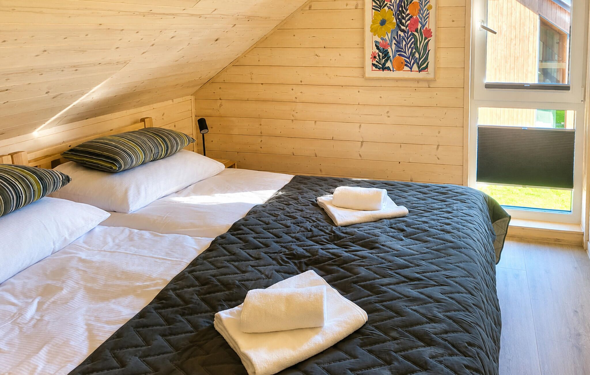 Ein Schlafzimmer mit zwei Betten, Holzwänden, einem großen Fenster und einem Bild an der Wand.