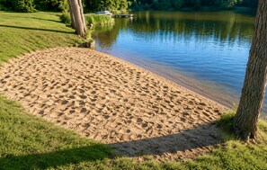 Una playa arenosa con un lago tranquilo, un muelle y árboles.