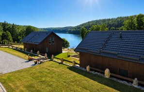 A wooden cabin with a sloped roof, a stone pathway, and a view of a lake surrounded by forest. - Cozy home in Lipnica with WiFi (Lipnica)