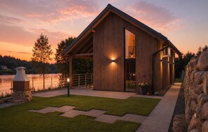 A modern wooden cabin with a glass door, a stone fireplace, and a view of a lake at sunset. - Cozy home in Lipnica with WiFi (Lipnica)