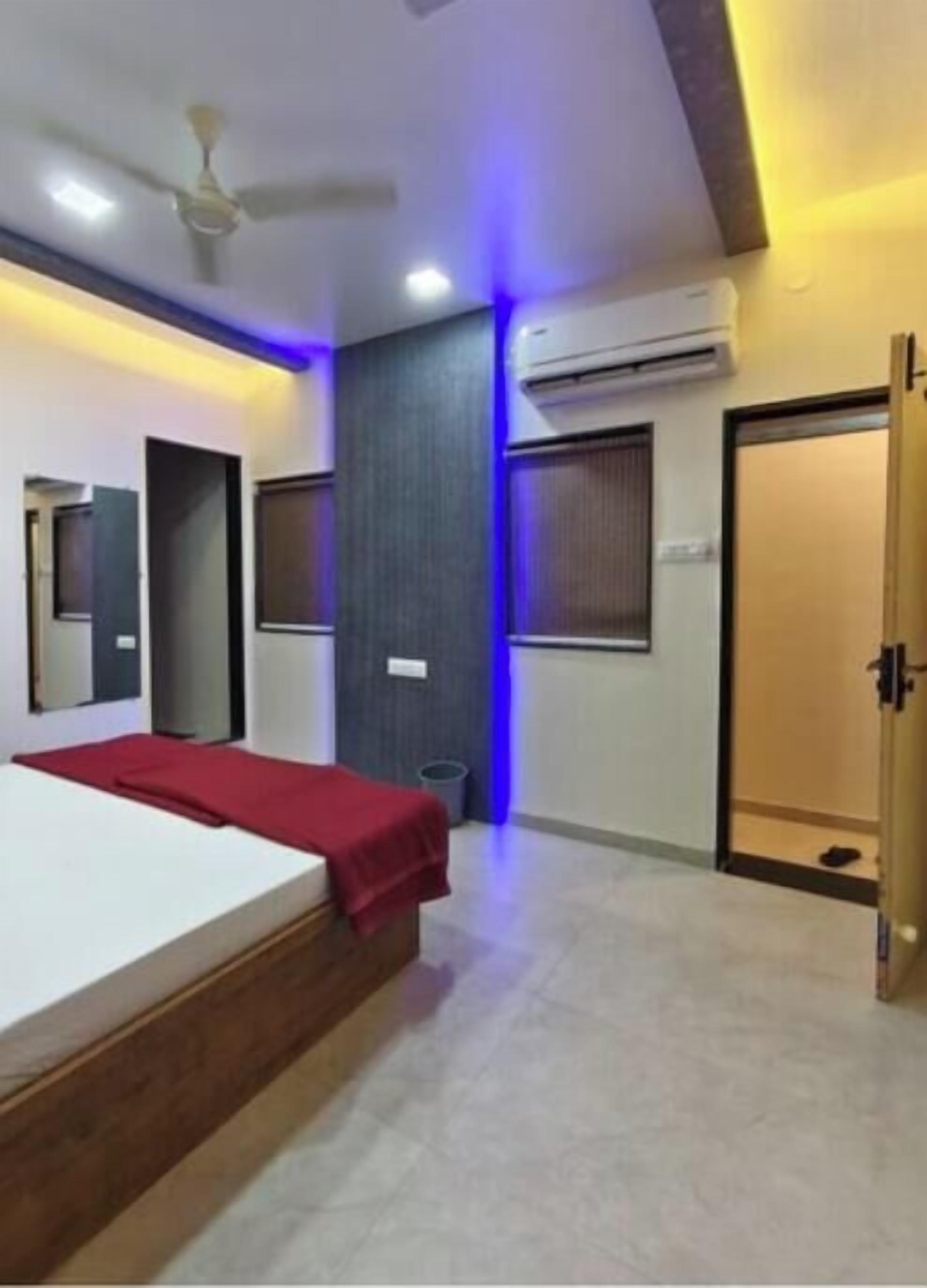 A hotel room with a bed, a ceiling fan, an air conditioning unit, a door, and a small trash bin.