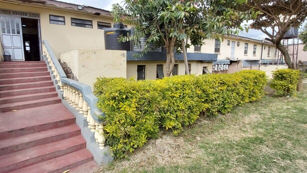 A building with a staircase leading to a door, surrounded by greenery and a water tank. - Crown Accomodation (Narok)