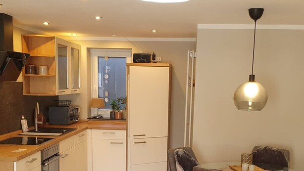 A modern kitchen with wooden cabinets, a built-in oven, and a dining area with a glass table and chairs.