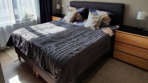 A bedroom with a large bed, a nightstand, a lamp, and a window with sheer curtains.