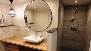 A modern bathroom with a vanity, a large mirror, a shower with a handheld showerhead, and recessed ceiling lights.